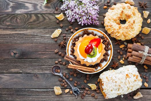 Rustic wooden background with different pastries - peanut and fruit tarts, marzipan bun. Different spices - cinnamon, walnuts, peanuts, ginger. Top view of tasty desserts. Place for text.