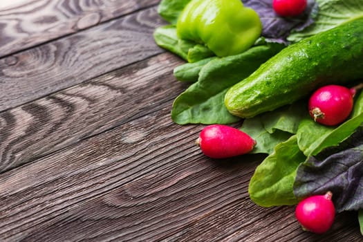 Fresh ingredients for salad - sorrel leaves, radishes, cucumber, sweet pepper on wooden background. Rustic table with tasty vegetables. Place for text.