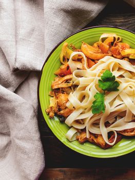 Green plate with tasty fettuccine bolognese and tomato sauce. Top view on wooden table, napkin and bowl with pasta. Italian cuisine.