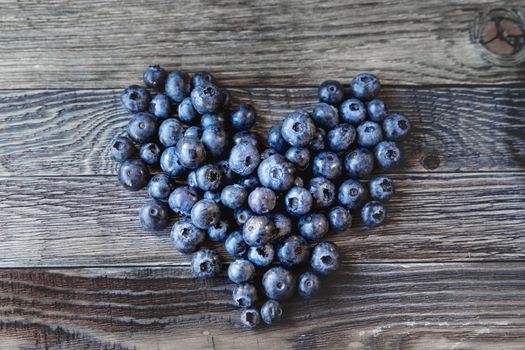 Blueberries on rustic wooden cozy background. Fresh-gathered berries full of vitamins, good for diet nutrition and healthy meals. Heart as a symbol of love and romance.