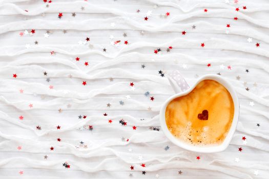 Cup of hot coffee with cinnamon heart. Winter and Valentine's Day fabric background with sparkling silver and red confetti.