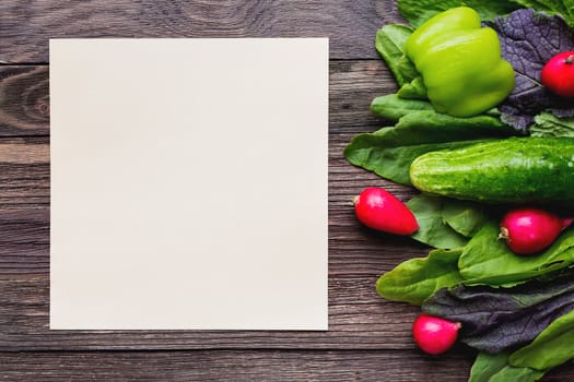 Fresh ingredients for salad - sorrel leaves, radishes, cucumber, sweet pepper on wooden background. Rustic table with tasty vegetables. Clear paper for text.