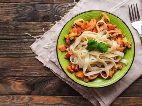 Green plate with tasty fettuccine and tomato sauce. Top view on wooden table, napkin and bowl with pasta. Italian cuisine.