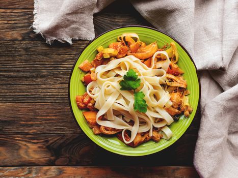 Green plate with tasty fettuccine bolognese and tomato sauce. Top view on wooden table, napkin and bowl with pasta. Italian cuisine.