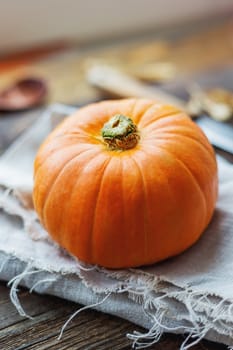 Fresh orange pumpkin on wooden table. Homespun napkin and rustic cutlery on background.