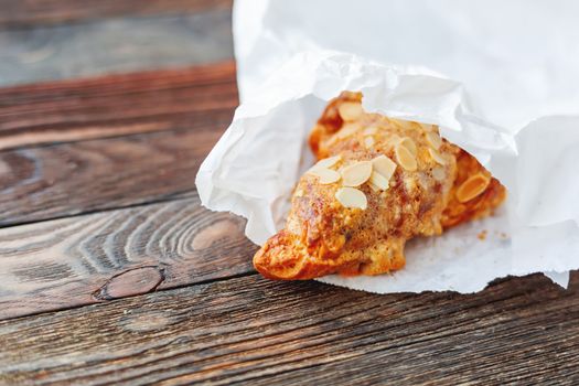 Tasty croissant in white paper bag on table. Rustic wooden background with sweet dessert.