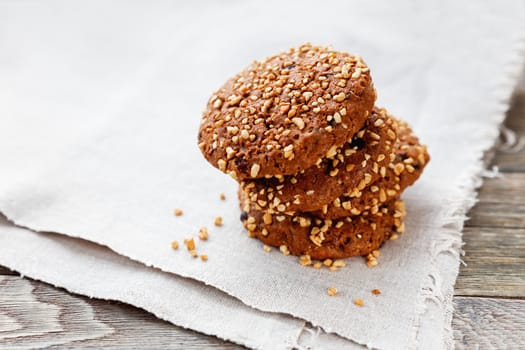 Chocolate cookies stacked on the edge of homespun napkin. Oat cookies with nuts, sesame and chocolate on wooden background.