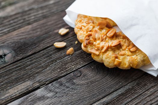 Tasty tart with peanuts in white paper bag. Rustic wooden background with sweet dessert.