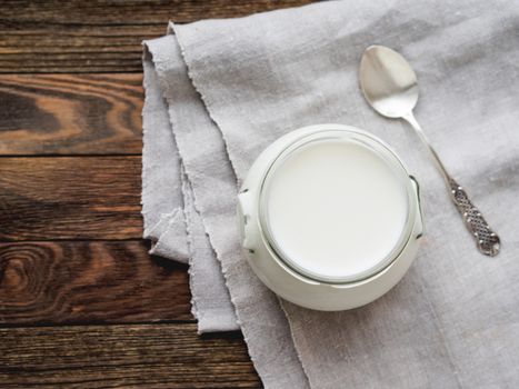 Natural homemade yogurt in a glass jar. Healthy food for breakfast. Linen tablecloth and silver spoon on on wooden table.