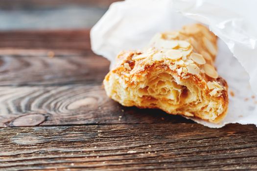 Tasty croissant in white paper bag on table. Rustic wooden background with sweet dessert.