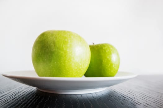 Two fresh green apples on white plate.