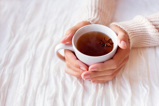Women holds a cup of hot tea with anise star. Cozy morning at home.