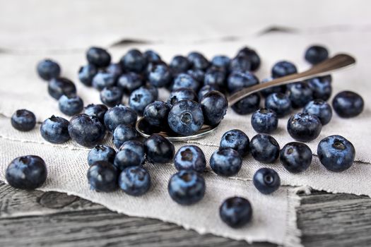 Blueberries lie on a homespun tablecloth and in metal spoon. Rustic cozy background with healthy food. Fresh-gathered berries full of vitamins, good for diet nutrition and healthy meals.