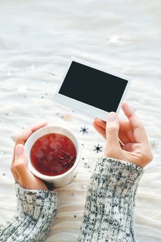 Woman holds a cup of tea and photo. Winter fabric background with sparkling silver snowflakes. Empty photo frame for your text or picture.