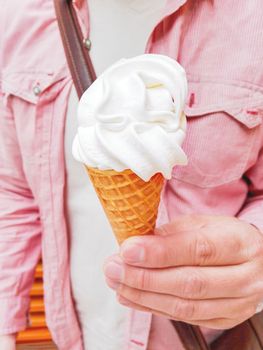 Man in light red shirt holds a tasty waffle cone with ice-cream.