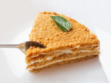 White plate with honey cake. Tasty dessert with sour cream. Metal spoon with a little bite of cake.