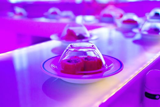 Conveyor serving dishes. Neon-purple lights over the plates with the sushi rolls.