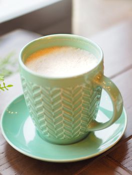 Porcelain aquamarine colored cup with cappuccino. Coffee mug on wooden table. Tasty hot beverage.