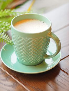 Porcelain aquamarine colored cup with cappuccino. Coffee mug on wooden table. Tasty hot beverage.