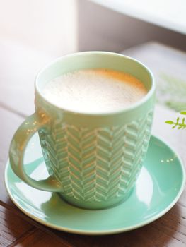 Porcelain aquamarine colored cup with cappuccino. Coffee mug on wooden table. Tasty hot beverage.