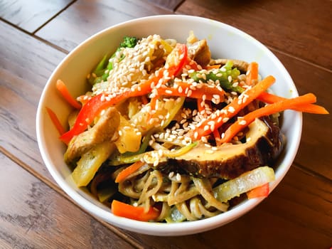 Asian cuisine - noodle in sauce with stir fried vegetables and chicken meat in white bowl. Close up.