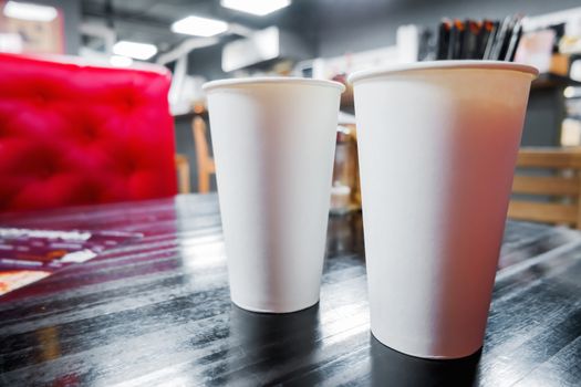 Two clear white paper glasses with coffee on cafe table. Industrial cafe interior. Mock up, place for text.