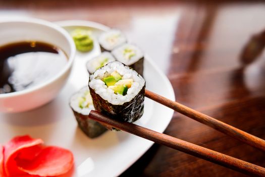 Rolls in nori seaweed with avocado, pickled ginger and soy sauce. Asian cuisine, traditional dish - sushi.