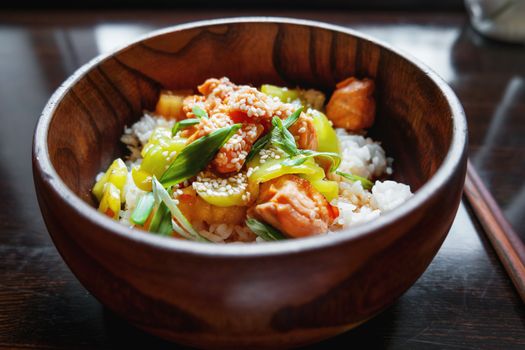 Asian cuisine - rice in sauce with stir fried vegetables, pineapple and salmon. Wooden bowl with chopsticks.