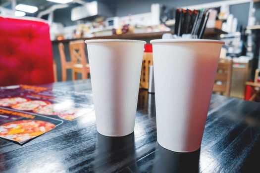 Two clear white paper glasses with coffee on cafe table. Industrial cafe interior. Mock up, place for text.