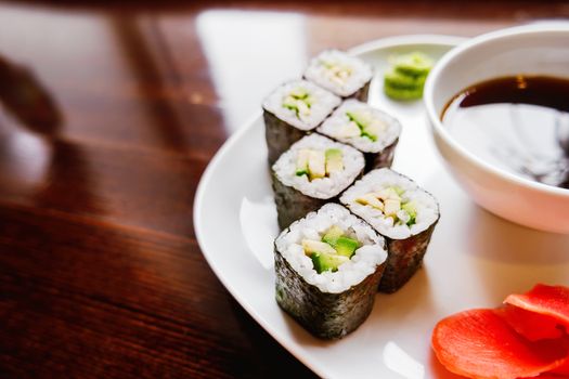Rolls in nori seaweed with avocado, pickled ginger and soy sauce. Asian cuisine, traditional dish - sushi.