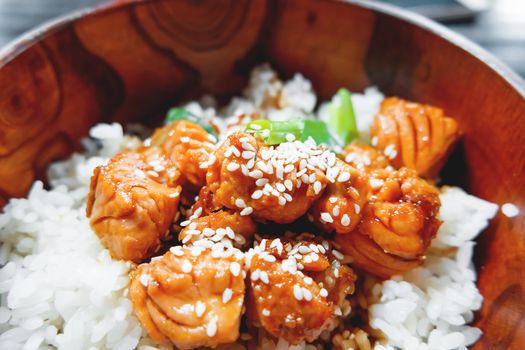 Asian cuisine - rice in sauce with stir fried vegetables and salmon in wooden bowl. Close up.