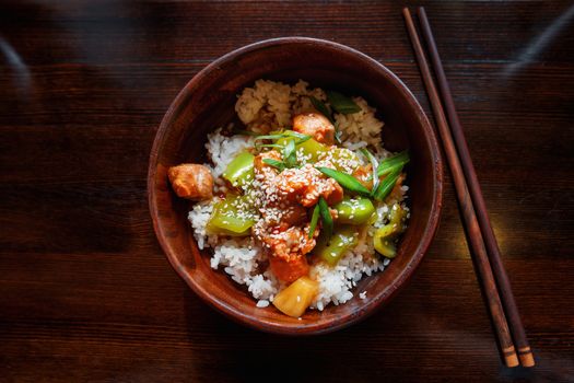 Asian cuisine - rice in sauce with stir fried vegetables, pineapple and salmon. Wooden bowl with chopsticks.