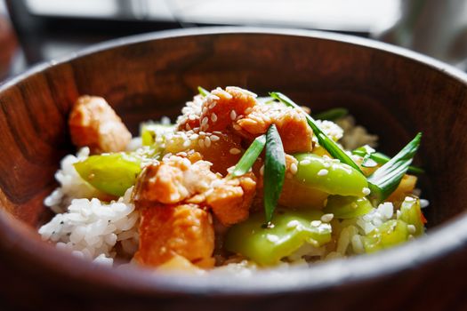 Asian cuisine - rice in sauce with stir fried vegetables, pineapple and salmon in wooden bowl. Close up.