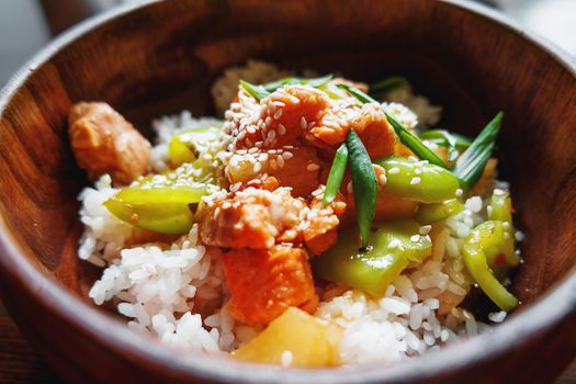 Asian cuisine - rice in sauce with stir fried vegetables, pineapple and salmon in wooden bowl. Close up.