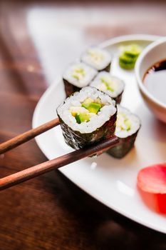 Rolls in nori seaweed with avocado, pickled ginger and soy sauce. Asian cuisine, traditional dish - sushi.
