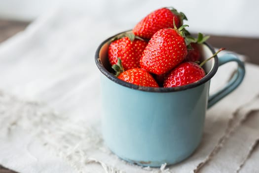 Fresh juicy strawberries in old rusty mug. Rustic wooden background with homespun napkin.