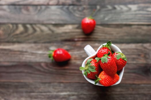 Fresh juicy strawberries in cup shaped as a heart, symbol of love. Rustic wooden background. Top view, place for text.