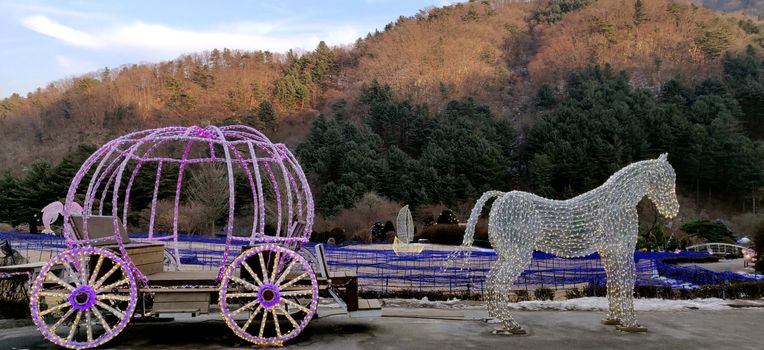 A cinderella fairy pumpkin horse cart fitted with LED lights again backdrop of beautiful mountains and glorious evening sun in garden of morning calm in South Korea.