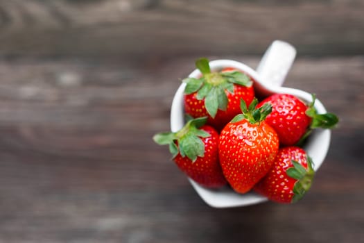 Fresh juicy strawberries in cup shaped as a heart, symbol of love. Rustic wooden background. Top view, place for text.