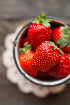 Fresh juicy strawberries in old rusty mug. Rustic wooden background with hand made crochet napkin. Top view, place for text.