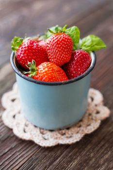 Fresh juicy strawberries in old rusty mug. Rustic wooden background with hand made crochet napkin.