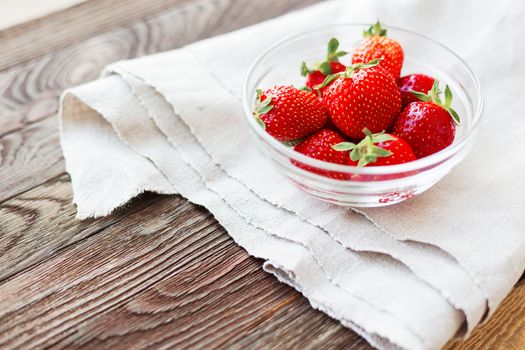 Fresh juicy strawberries in glass bowl. Rustic background with homespun napkin. Place for text.