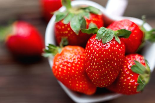 Fresh juicy strawberries in cup shaped as a heart, symbol of love. Rustic wooden background. Top view, place for text.