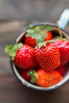 Fresh juicy strawberries in old rusty mug. Rustic wooden background. Top view, place for text.