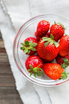 Fresh juicy strawberries in glass bowl. Rustic background with homespun napkin. Top view.