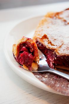 Cherry strudel on a saucer with a spoon. Piece of fresh tasty dessert with berries.