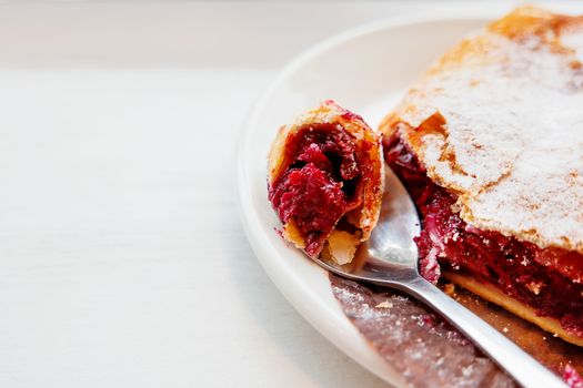 Cherry strudel on a saucer with a spoon. Piece of fresh tasty dessert with berries.