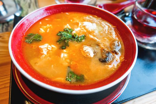 Asian cuisine - Tom kha kai or Thai coconut soup with chicken meat, rice, mushrooms, ginger and lemongrass in red bowl. Close up.