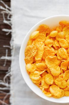 Tasty corn flakes in bowl. Rustic wooden background with homespun napkin. Healthy crispy breakfast snack. Top view, flat lay.