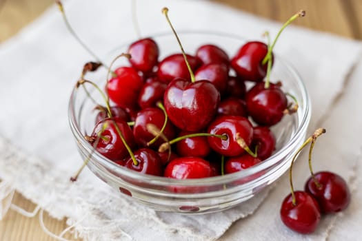 Fresh juicy sweet cherries in glass bowl. Rustic background with homespun napkin.